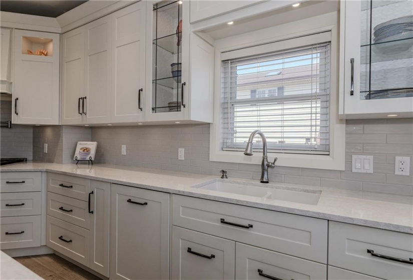 A large under mount double sink and touch sensitive faucet. Not shown is the waste and recycling centre below. Glass front cabinetry and pot lighting allow you to feature your decorative tableware.