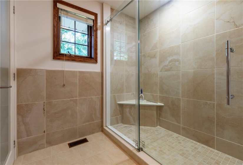 A low profile glass walk-in shower features bench seating. It's own linen closet separate from the large walk-in closet.