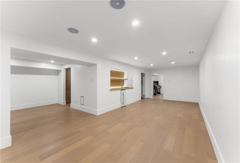 Media room. Wine bar on left, wet bar mid-frame. Large bathroom rear left. Bedroom/office/den rear center. White oak flooring throughout. Utility room.