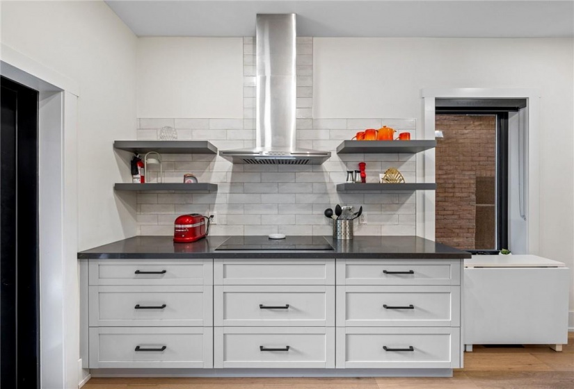 Kitchen on main-floor: built-in cook-top with hood vent, built-in oven, quartz countertops, patterned subway tile backsplash