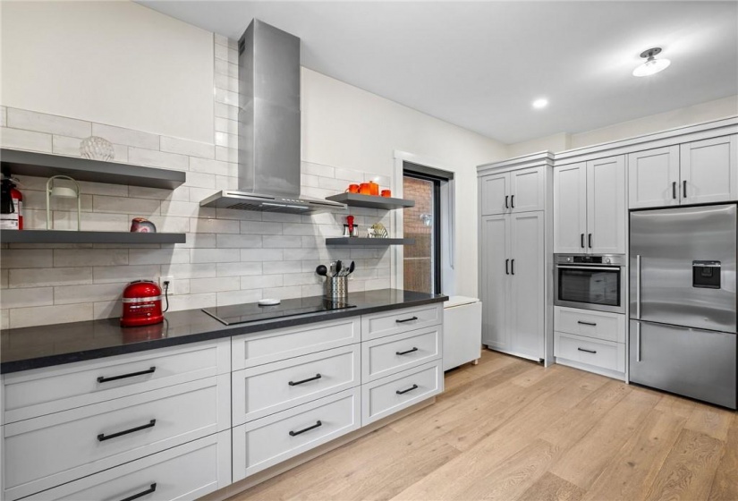 Kitchen on main-floor: built-in cook-top with hood vent, built-in oven, quartz countertops, patterned subway tile backsplash